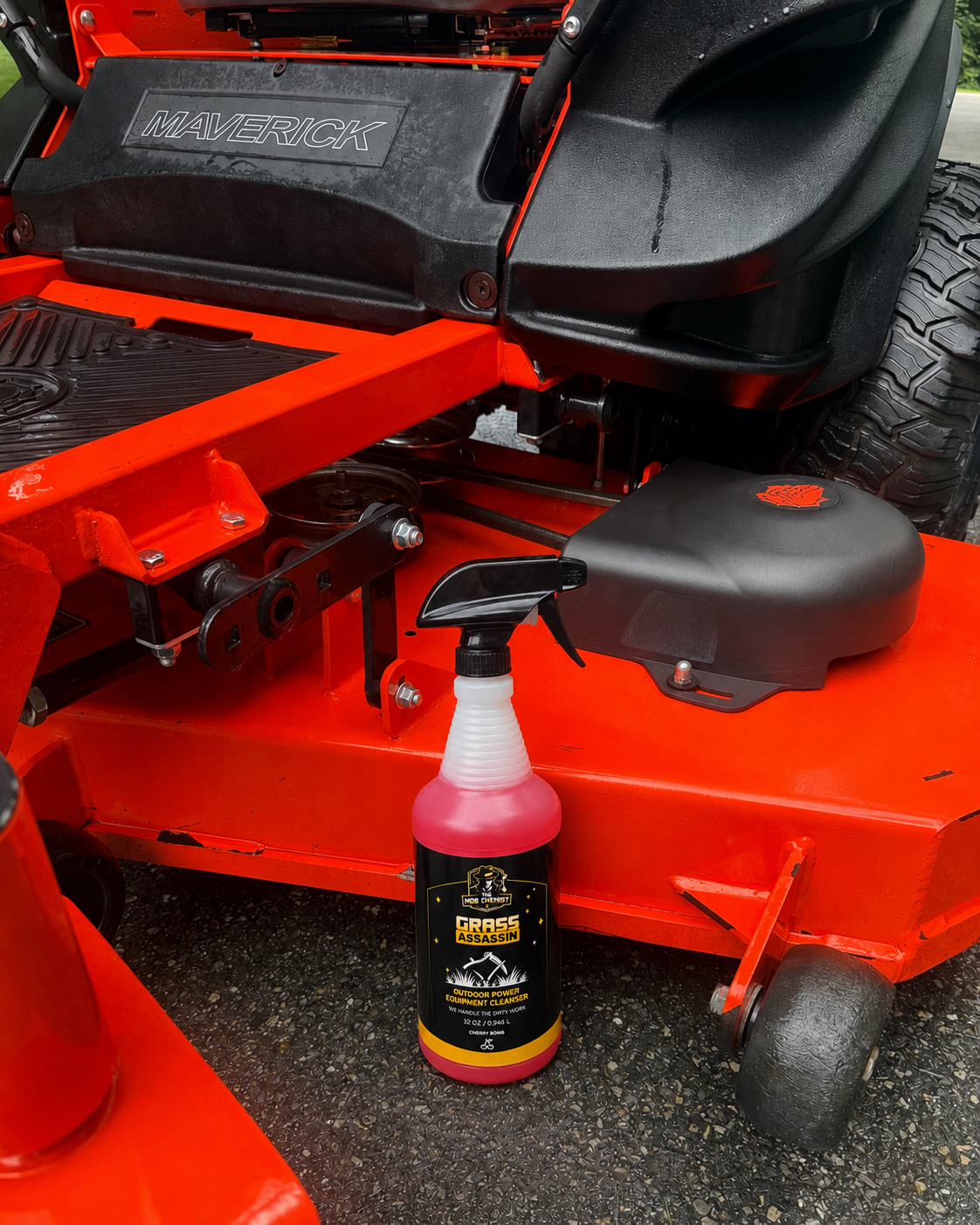A bottle of Grass King Purple Grass Killer herbicide with pink liquid, placed on the ground next to a red riding lawn mower.